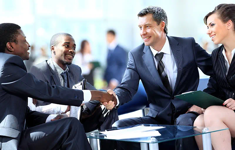 Expertise Two business people shaking hands while their assistants smile.