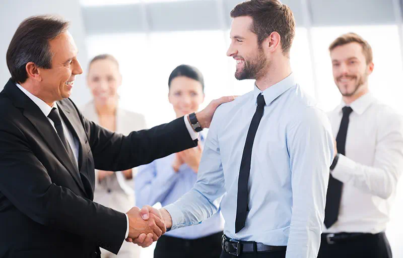 Integrity A manager shakes the hand of a newer agent while others look on and clap.