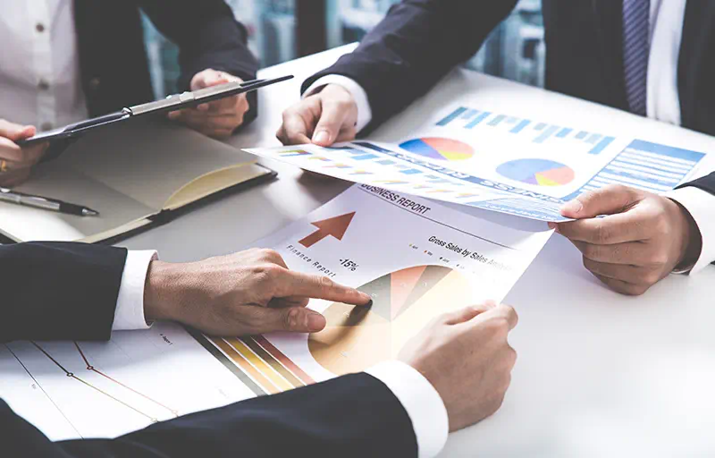 Marketing Strategy Three business people reviewing reports with charts and graphs.