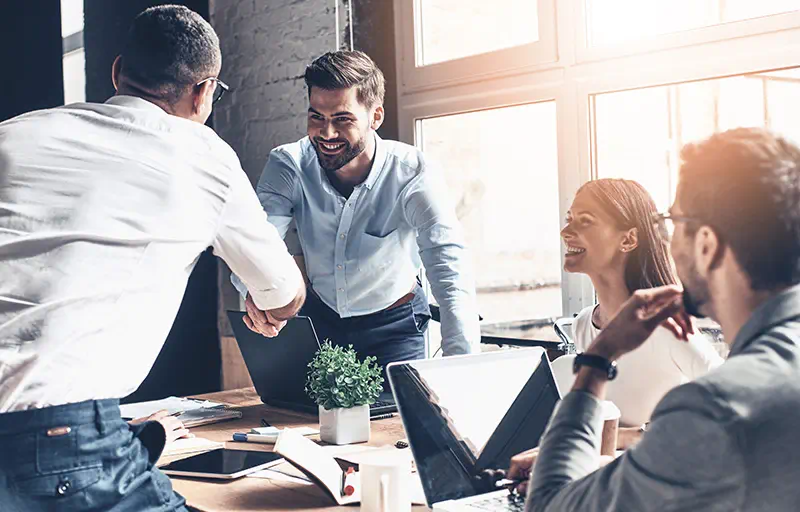 Two business men shaking hands while two others smile and look on.
