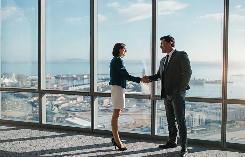 Two business people shaking hands in an empty office space.