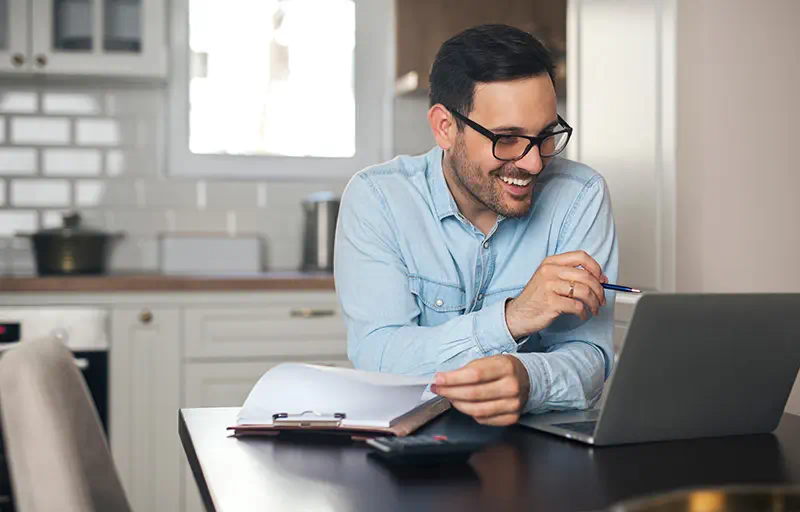 A business man smiles at his laptop while working at home.