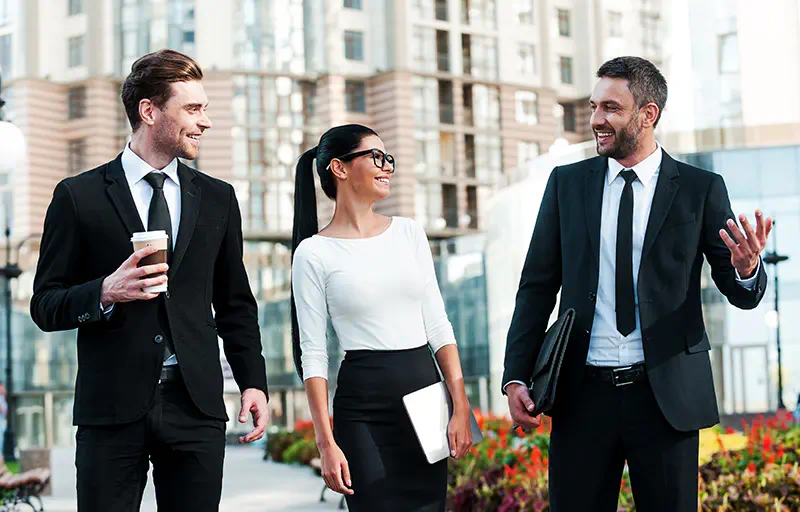 Three young business people talking while walking outside of an office building.