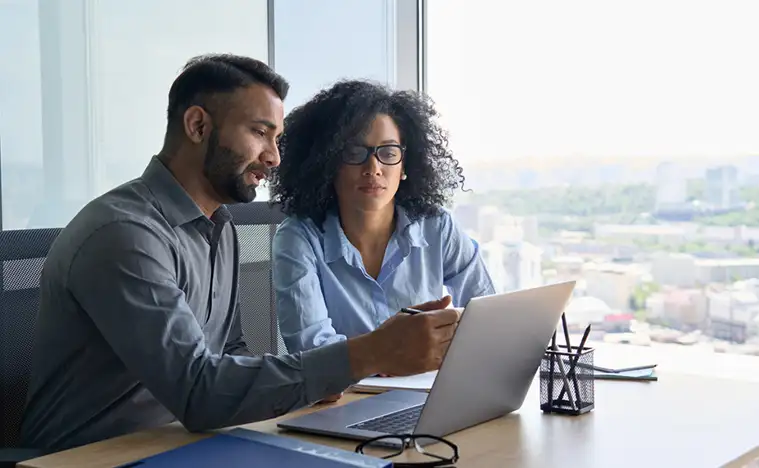 Two business people look over a laptop.